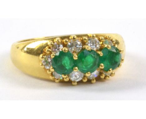 An 18ct yellow gold ring, set with three emerald round cut stones surrounded by a border of round cut diamonds in claw settin