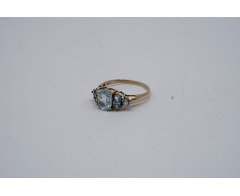 A blue topaz ring, comprising a central oval stone of approx. 8 mm x 6 mm framed by trios of smaller stones, claw set on 9 ct