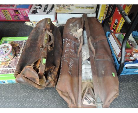 A vintage cricket bag containing pads and gloves along with a similar gladstone bag
