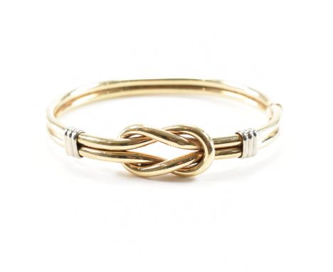 A vintage two tone gold knot design bangle bracelet. The bracelet of tubular form with white gold banding and a hinged openin