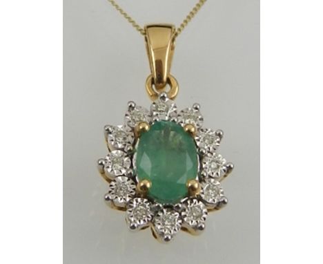 An 18 carat yellow gold, emerald, and diamond oval cluster pendant, suspended on a 9 carat yellow gold chain. 