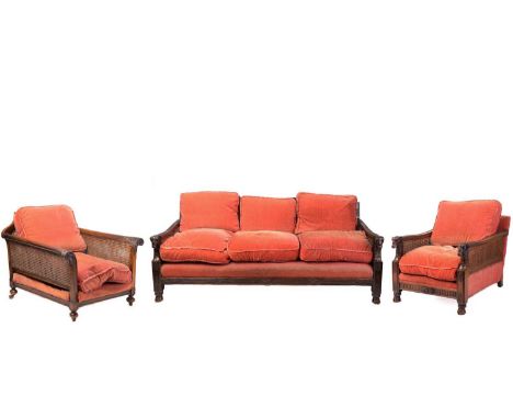A carved walnut three-seat Bergere sofa and matching club chair, early 20th century, each with carved rams head arm terminals