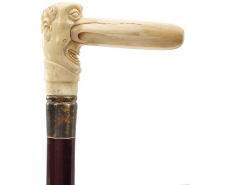 AN EARLY 20TH CENTURY WALKING STICK, the marine ivory handle carved as a gentleman with a large nose, above metal collar, tap