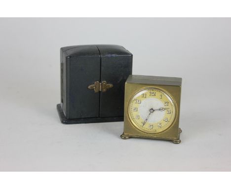 An early/mid 20th century travelling alarm clock, square gilt body with circular dial and Arabic numerals in two-door black c