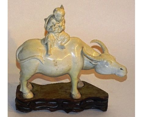 A Chinese blanc de chine figure of a seated boy playing flute on buffalo, raised on hardwood stand, 23cm high   CONDITION REP