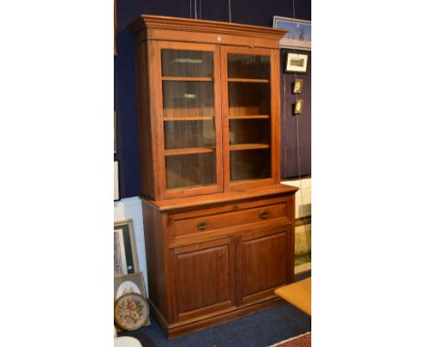 A pine bookcase on secretaire chest, circa early 20th century, with moulded cornice above two glazed doors enclosing shelved 