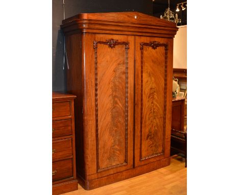 A Victorian flame mahogany wardrobe, with moulded cornice above two panelled doors, decorated with moulded scroll mounts, enc