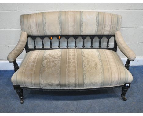 A LATE VICTORIAN EBONISED SOFA, with stripped upholstery, swept open armrests, spindle back supports, raised on turned front 