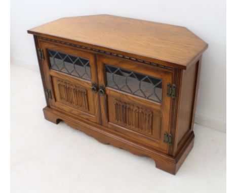 A reproduction carved oak TV / entertainment unit - with a pair of part-glazed doors with linenfold carved panels, enclosing 