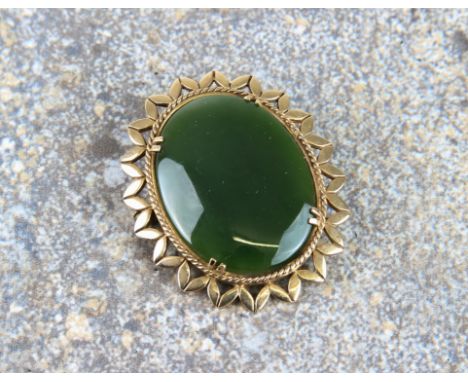 A 9ct yellow gold and jade brooch - stamped '9CT', the oval 31 x 23mm. stone within a pierced, petalled border, 4cm. long, gr