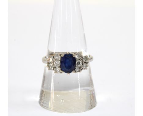 A Sapphire and diamond cluster ring, the claw set sapphire flanked by five smaller diamonds, set in white gold, inner band st