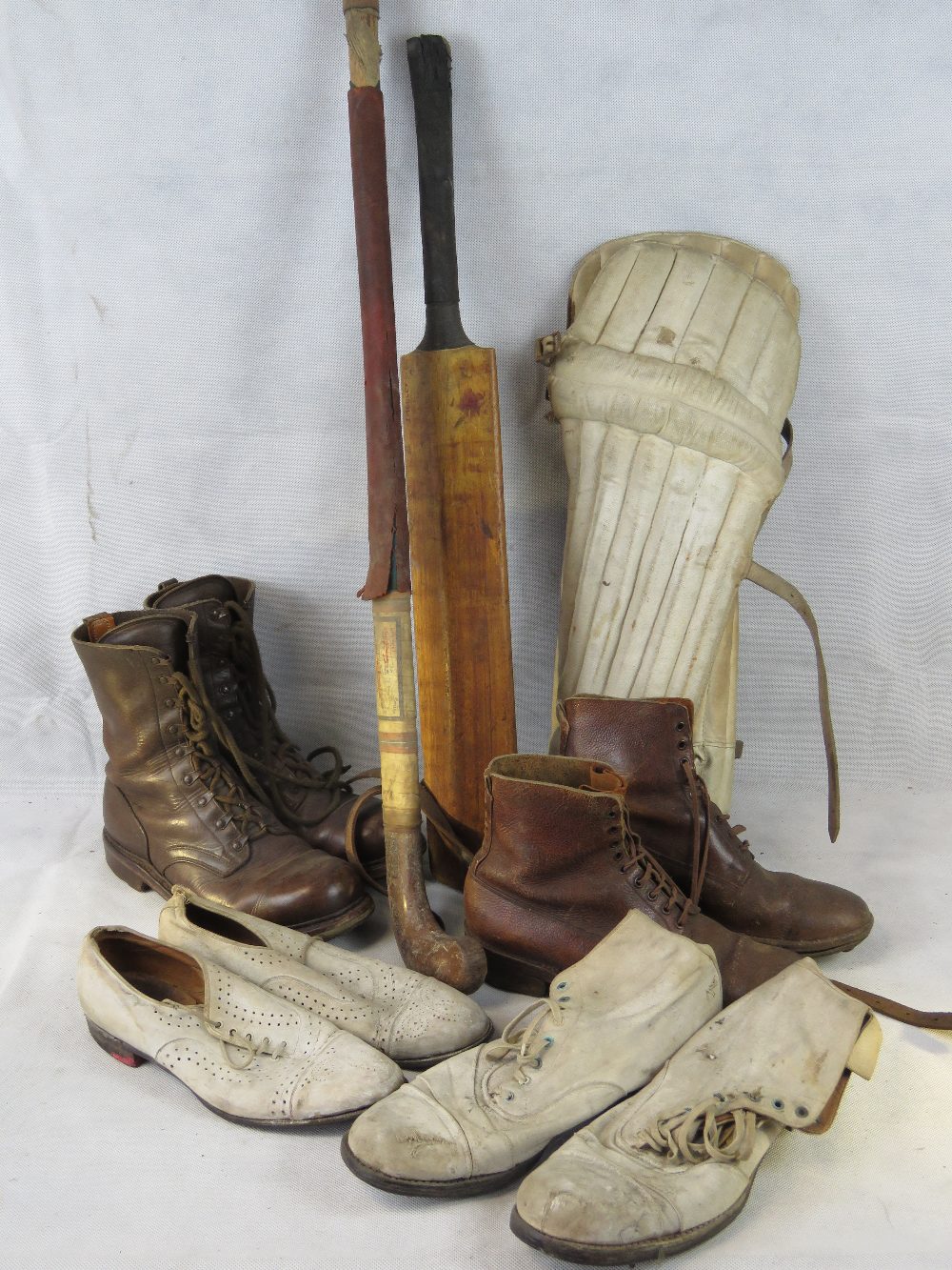 A pair of vintage cricket pads, cricket bat, a hockey stick and two
