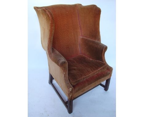 A George III mahogany upholstered wing back armchair, with serpentine back, shaped wings, scroll arms and cushion seat, on mo