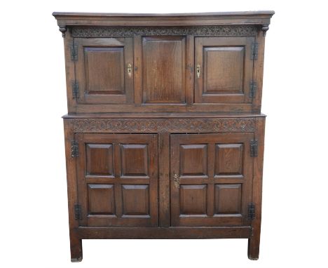 A Queen Anne oak press cupboard, circa 1700, of panelled form and in two sections, with entwined scroll carving, the upper se