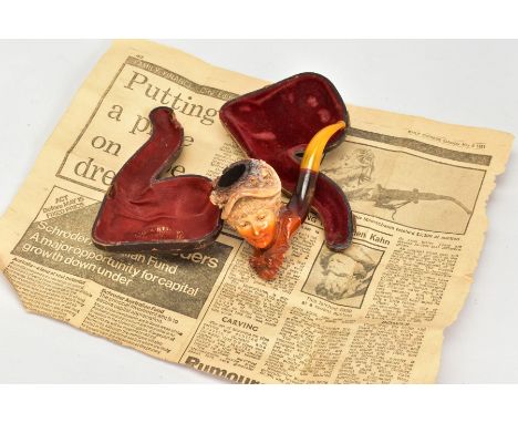 A MEERSCHAUM CASED PIPE, in the form of a lady with floral hat, with an amber coloured stem, together with case and newspaper