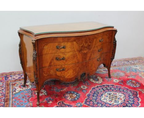 A continental burr walnut and mahogany commode with a serpentine top above three long drawers on leaf carved feet and sides, 