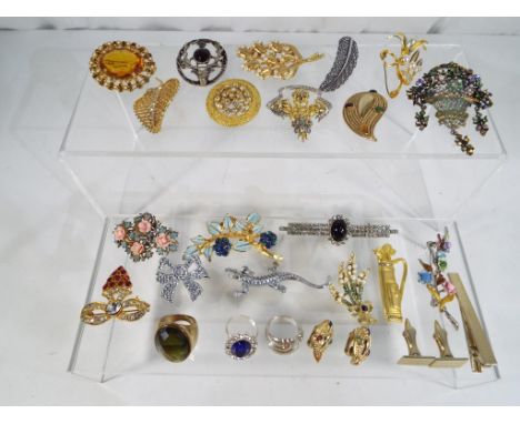 A wooden box containing nineteen decorative brooches, three rings, a pair of earrings, a pair of cufflinks and a tie-pin, all