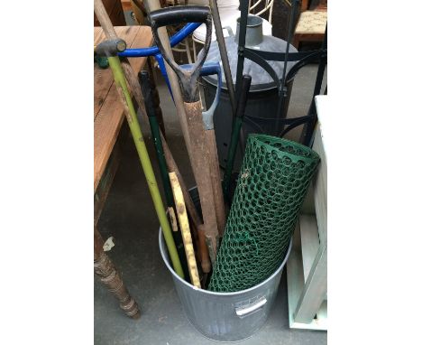A galvanised metal dustbin containing garden tools and a galvanised metal compost bin