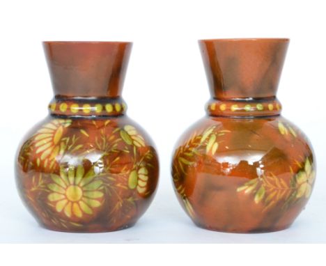 Linthorpe Pottery - A pair of small vases of globe and shaft form decorated with white slip daisies and foliage against a bro