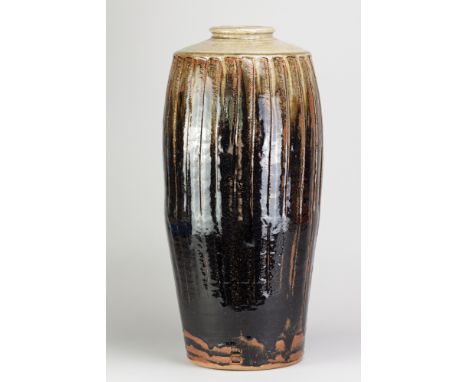 JIM MALONE (born 1946); a tall stoneware fluted bottle covered in tenmoku breaking to kaki glaze with green ash top, impresse