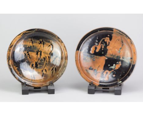 JIM MALONE (born 1946); a near pair of stoneware dishes covered in tenmoku and kaki glaze with wax resist decoration, impress