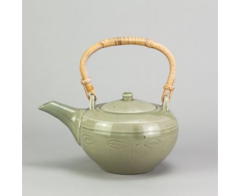 BERNARD LEACH (1887-1979) for Leach Pottery; a stoneware teapot with cane handle covered in celadon glaze with incised decora