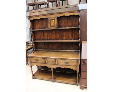 A traditional style oak dresser and rack, joined, the rack with two shelves and a single door, the base with three drawers an