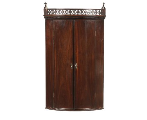 A GEORGE III BOW FRONTED MAHOGANY CORNER CUPBOARD, C1780&nbsp;&nbsp;the fretwork frieze with thistle terminals, the painted i