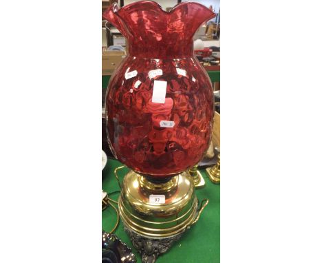 A large Victorian oil lamp with cranberry glass shade on a brass reservoir to pierced scrollwork feet (converted to electrici