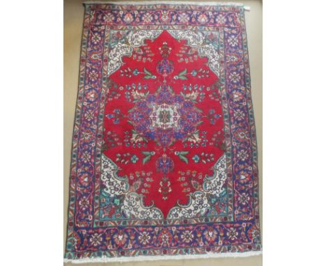 An Oriental carpet, the central floral decorated medallion in cream, blue, red and green on a red ground with cream and blue 