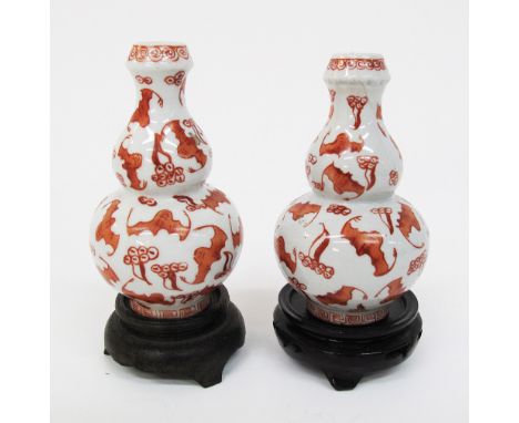 A pair of Chinese double gourd vases hand painted in iron red with bats, H10cm, standing on hardwood bases, unmarked, one wit