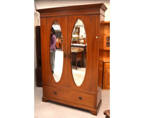 An Edwardian mahogany inlaid two-door wardrobe, oval mirror inserts to door above long drawer to base on bracket supports, 19