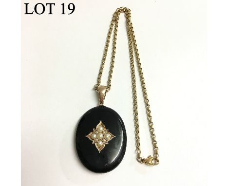 A Victorian onyx pendant set with seven seed pearls and split pearls with locket back and set in gold with attached gold chai