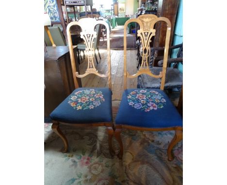 A pair of Edwardian dining chairs, having Art Nouveau inlaid decoration over tapestry seats on front cabriole supports.