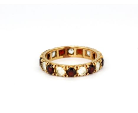 A yellow metal (tested 9ct gold) garnet and white stone set full eternity ring, (K).