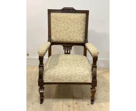 An Edwardian mahogany framed open armchair, the crest rail carved with floral swags, upholstered seat and back, moving on cer