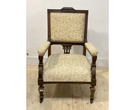 An Edwardian mahogany framed open armchair, the crest rail carved with floral swags, upholstered seat and back, moving on cer