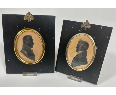 Two 19thc shilouette portrait miniatures on coloured paper in oval gilt metal mounted black framed panels with acorn ring sur