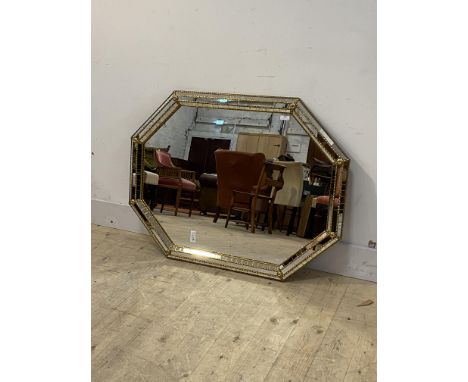 A floral embossed gilt brass and sectional glass framed wall hanging mirror of octagonal outline, 101cm x 76cm