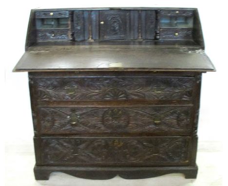 An Antique dark oak carved bureau, the fall flap opening to reveal drawers, cupboard and pigeon holes, over two short and thr