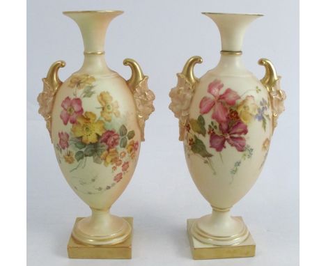 A pair of Royal Worcester blush ivory vases, decorated with floral sprays, with mask handles, raised on a pedestal, shape num