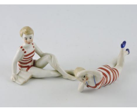A pair of Art Deco style porcelain figures, depicting boy and girl bathers in striped swim suits.