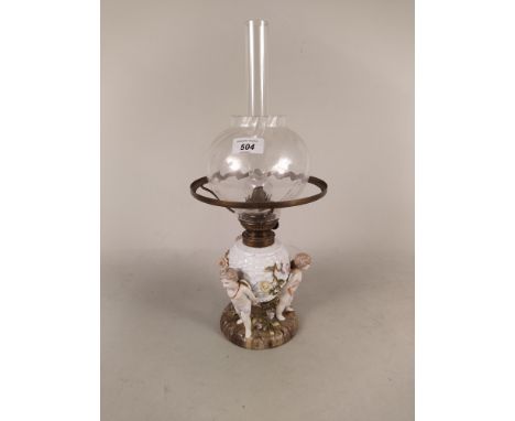 A late 19th Century Schierholz porcelain oil lamp of three cupids supporting basket moulded reservoir with later clear glass 