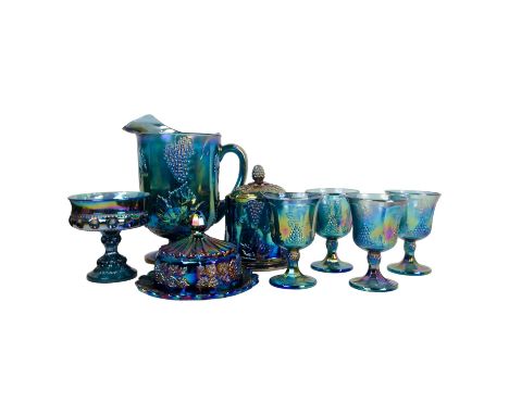 A collection of blue carnival glass - iridescent and moulded with grapes and vines, including a jug, four glasses, biscuit ba