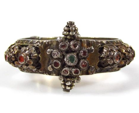 An Indian bangle, of elaborate design, with raised sections set with precious stones (lacking) unmarked metal, 8cm wide. (AF)