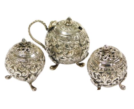 An early 20thC Anglo Indian three piece condiment set, embossed with scrolling leaves, raised on three leaf-capped paw feet, 