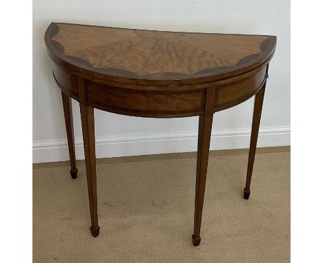An Edwardian satinwood demi-lune fold-over card table, enclosing a green baize surface and raised on tapering supports, heigh