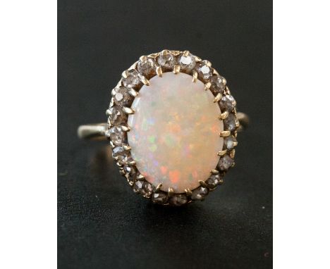 An opal and diamond ring, with a central oval fire opal displaying orange, red, green and blue within a border of twenty old 