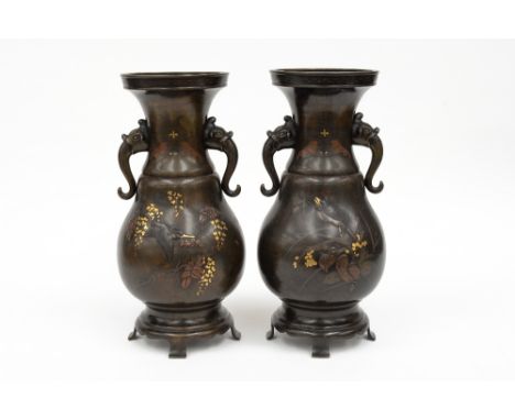 A pair of Japanese shakudo/inlaid bronze vases, Meiji period, each of organic baluster form with mask and tongue handles, on 