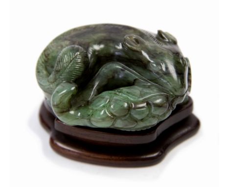 A very fine Chinese green jade carving of a squirrel, Qing Dynasty, curled up on a vine leaf, a cluster of grapes in its gras